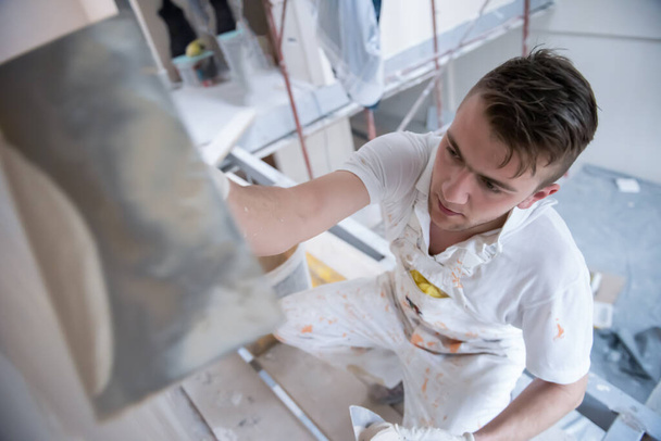 young professional construction worker plastering on gypsum walls inside the new big modern two levels apartment - Fotografie, Obrázek