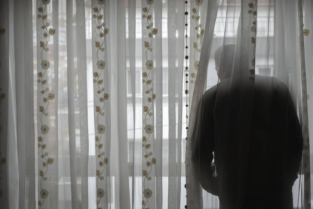 Hombre mayor obedeciendo al toque de queda mirando a la calle vacía desde su ventana
 - Foto, imagen