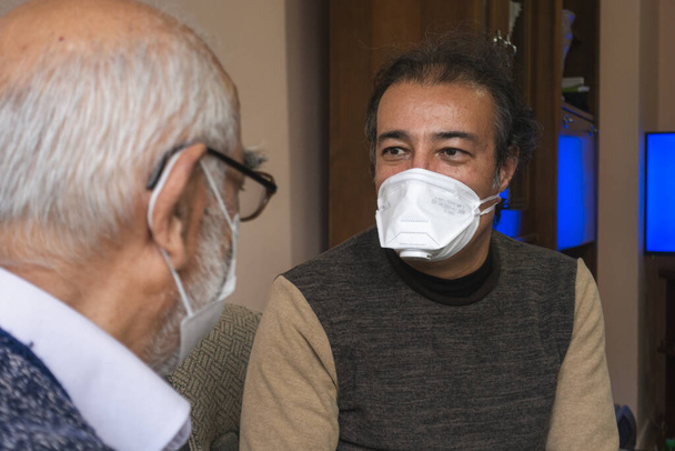 Maske takan kıdemli bir adam yaşlılarla konuşuyor. - Fotoğraf, Görsel