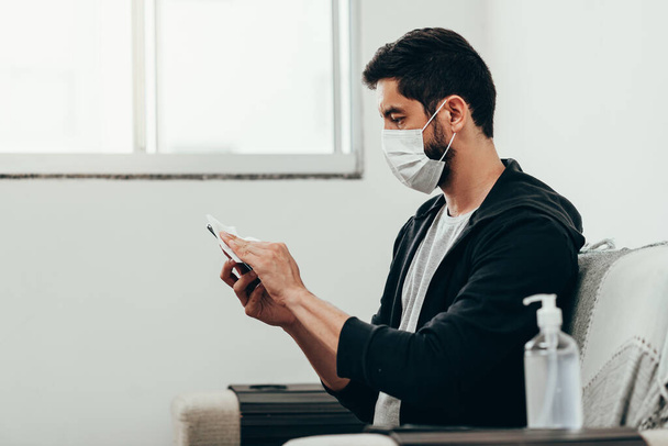 Coronavirus, covid-19 and quarantine concept. Man cleaning smartphone screen with alcohol or sanitizer. - Fotografie, Obrázek