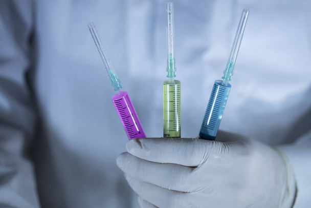 Ο γιατρός κρατάει τρία εμβόλια στο χέρι του. Εμβόλια σε κόκκινο και πράσινο χρώμα. Πυροβολισμοί στούντιο. Κλείσε.. - Φωτογραφία, εικόνα