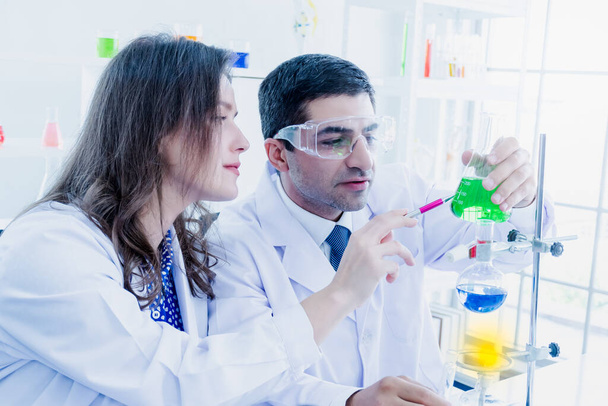Bliskowschodni naukowiec i biała piękna kobieta naukowiec analizują zielone rozwiązanie w błysku w laboratorium naukowym. - Zdjęcie, obraz