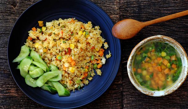 Высокий вид женщины рука приготовить еду для быстрого ужина, веганская еда с плотным жареным рисом с супом из овощей, как морковь, кукуруза, фасоль, вегетарианское блюдо в желтом, вкусная вьетнамская кухня
  - Фото, изображение