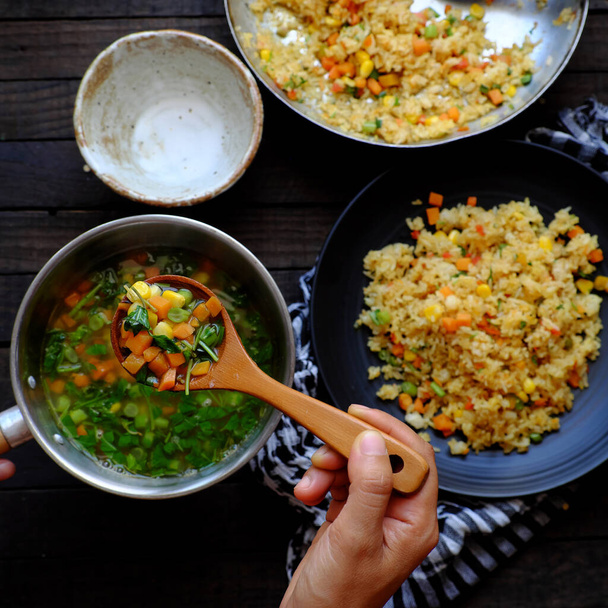Hohe Ansicht Frau bereiten Essen für das Abendessen, vegane Mahlzeit mit Pilaw gebratenem Reis und Suppe aus Gemüse wie Möhren, Mais, Saitenbohne, vegetarisches Gericht in gelb, köstliche vietnamesische Küche  - Foto, Bild
