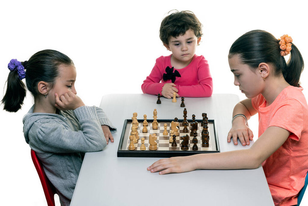 Kız kardeşler birlikte satranç oynuyorlar. Beyazlar üzerinde izole edilmiş. Çocuk konsantrasyonu kavramı. - Fotoğraf, Görsel