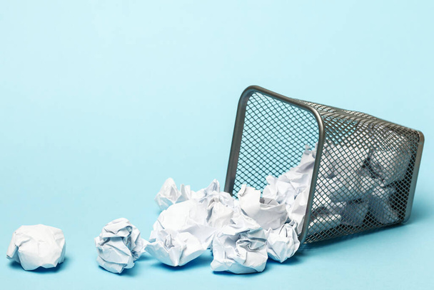 Overturned trash can with crumpled paper balls on a blue background. Closeup copy space. - 写真・画像