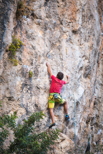 Ein starker Mann erklimmt eine Klippe. Der Kletterer bewältigt eine schwierige Kletterroute in natürlichem Gelände. Klettern in der Türkei. Schöner orangefarbener Felsen. - Foto, Bild