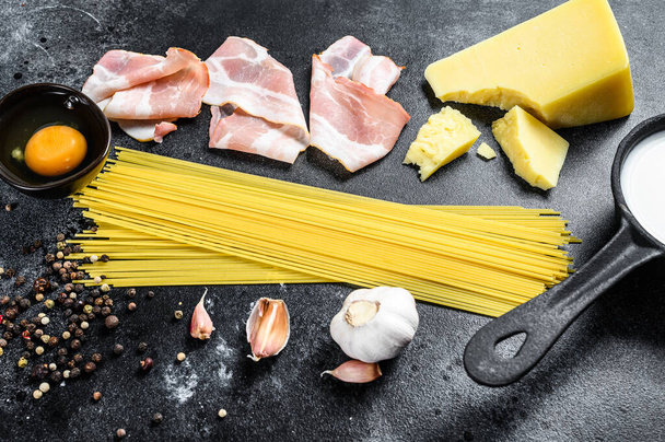 Ingrédients pour pâtes italiennes traditionnelles alla carbonara. Spaghettis non cuits, bacon pancetta, fromage parmesan, œuf. Fond noir. Vue du dessus. - Photo, image