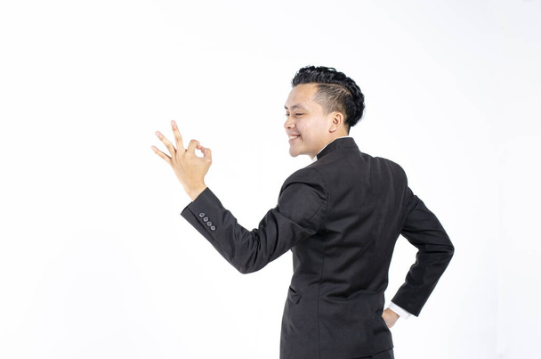 Portrait of a smiling businessman dressed in suit showing ok gesture against white background - Foto, afbeelding