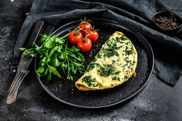 Egg omelet with spinach, served on a plate with tomatoes. black background. Top view. - Photo, Image