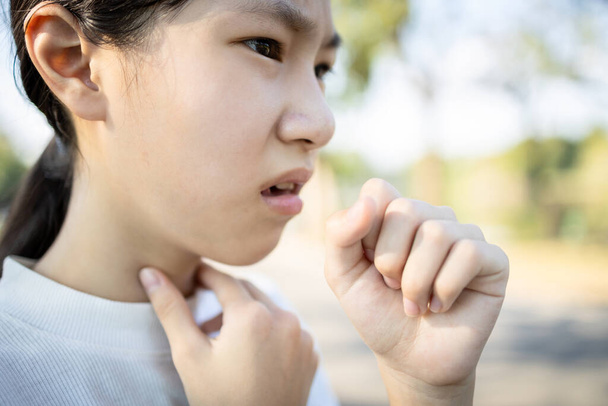Chora Azjatka ma chroniczny kaszel z zapaleniem migdałków, chore dziecko dotyka szyi z gorączką, ostry kaszel, ból gardła podrażnienie, głos jest chrypka z zimna, grypa, zakażenie dróg oddechowych - Zdjęcie, obraz