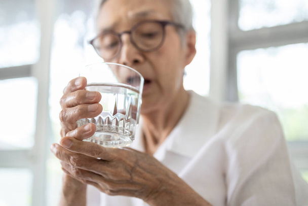 Mujer mayor sosteniendo vaso de agua, temblor de manos mientras bebe agua, paciente anciana con temblor de manos temblores corporales no controlados, síntoma de temblor esencial, enfermedad de Parkinson, trastornos neurológicos
 - Foto, imagen
