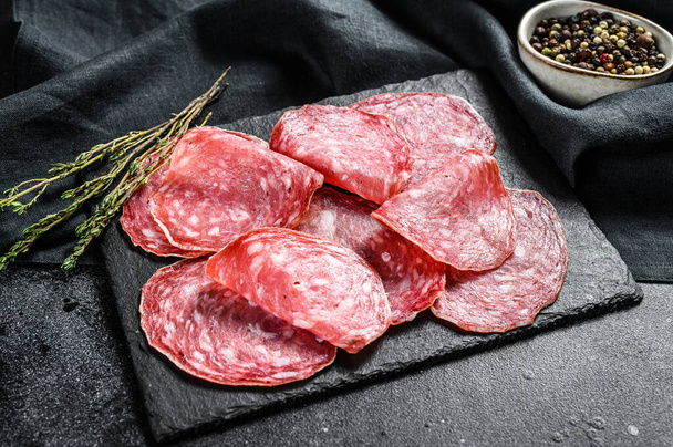 Salami sausage slices on a black chopping Board. Dark background. Top view. - Фото, зображення