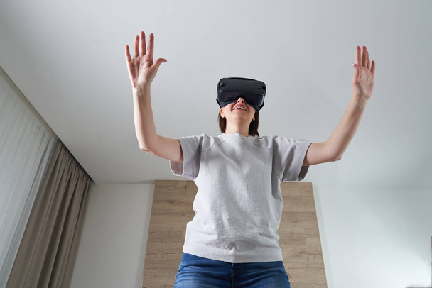 Ευτυχισμένη νεαρή γυναίκα που παίζει με γυαλιά VR σε εσωτερικούς χώρους, Εικονική πραγματικότητα έννοια με νεαρή κοπέλα που διασκεδάζει με γυαλιά ακουστικά, με χώρο αντίγραφο - Φωτογραφία, εικόνα