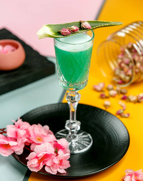 a glass of green cocktail garnished with aloe leave and dried rose buds - Фото, зображення