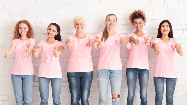 Nők rózsaszín pólóban Gesturing hüvelykujj fel, fehér háttér, panoráma - Fotó, kép
