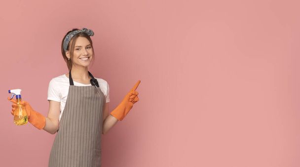 Smiling woman in apron holding sprayer and pointing at copy space - Фото, зображення