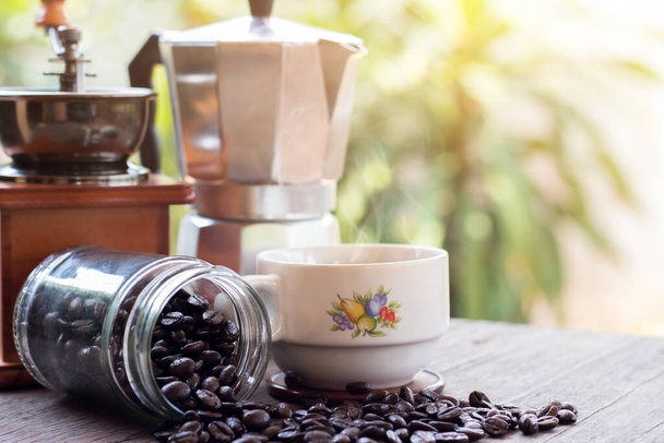 Ένα φλιτζάνι ζεστό καφέ espresso κούπες και ψητά φασόλια καφέ με moka κατσαρόλα τοποθετείται σε ξύλινο δάπεδο φόντο, πρωινό καφέ, επιλεκτική focu - Φωτογραφία, εικόνα