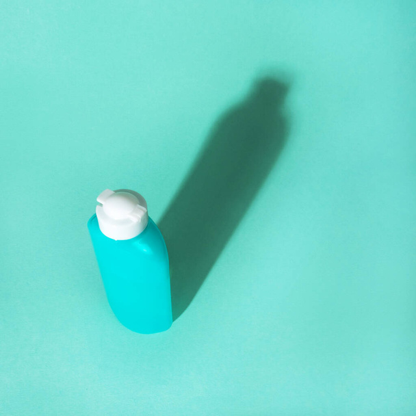 Kozmetik ambalaj plastik şişesi ve mavi arka planda dev gölgesi olan düz bir yatak. Plastiksiz konsept. - Fotoğraf, Görsel