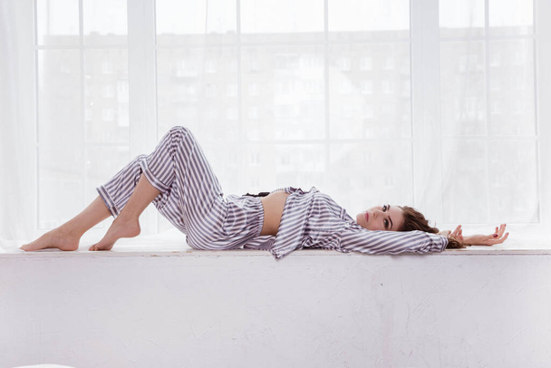 A beautiful woman is lying on the window in her pajamas. - 写真・画像