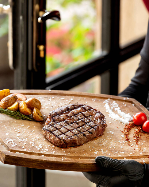 close up of waiter holding grilled steak served with roasted potato - 写真・画像
