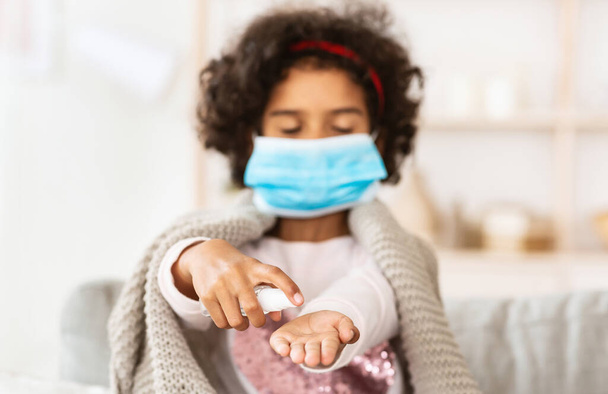 Koronavirová prevence. Malá afro americká dívka použití dezinfekci na ruce doma - Fotografie, Obrázek