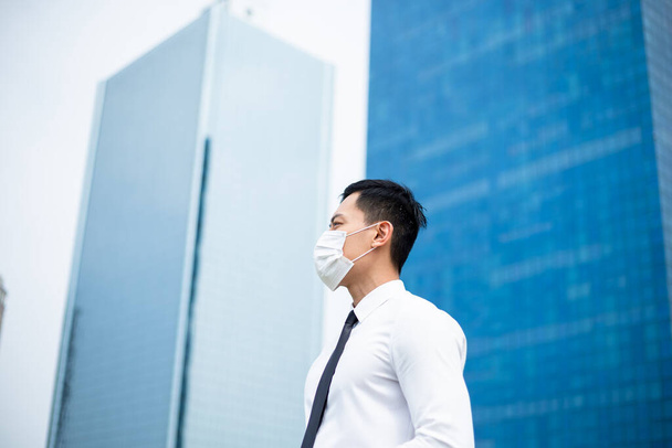 Homem de negócios asiático com uma máscara cirúrgica e ele olha ou pensa em algo na frente do prédio de escritórios
 - Foto, Imagem