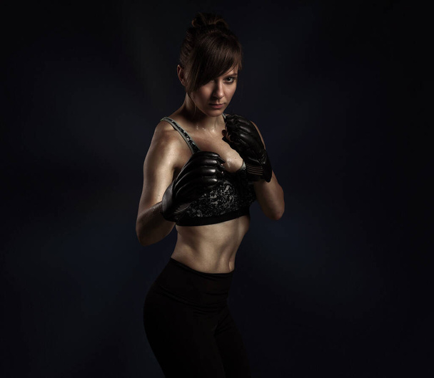 Concept de combat sportif avec espace de copie. Portrait de femme kickboxing en gants de boxe noirs et soutien-gorge de sport gris et culotte posant sur noir
 - Photo, image