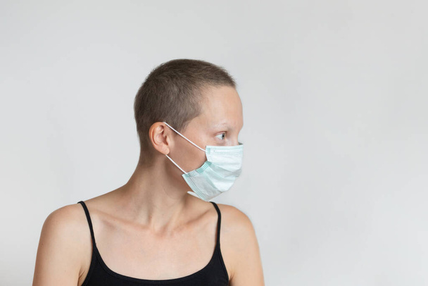 Profil widok z boku krótkie włosy młoda kobieta nosi ochronną maskę twarzy na twarzy przed ścianą w pomieszczeniach. Zapobieganie epidemii koronawirusów. Osoba kategorii wrażliwej. Świadomość pandemii wirusów. - Zdjęcie, obraz