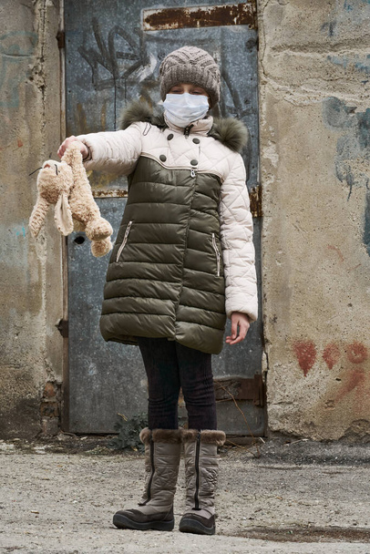 concept of epidemic and quarantine - a girl with a face mask and a cuddly toy alone on the street in the city - Photo, Image