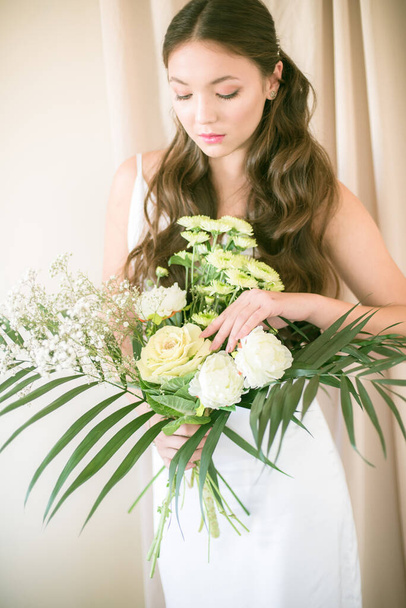 Delikatny bukiet ślubny w rustykalnym stylu białych kwiatów z zielonymi liśćmi w rękach panny młodej - Zdjęcie, obraz