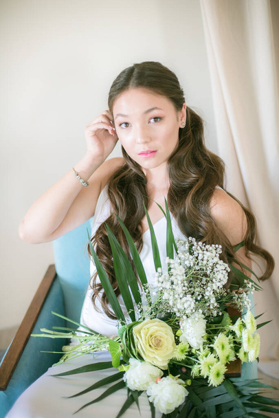 Cute przetargu młoda panna młoda o azjatyckim wyglądzie z długimi włosami w białej sukience z bukietem ślubnym kwiatów w studio - Zdjęcie, obraz