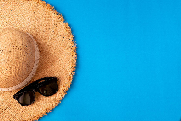 плоский простий дерев'яний капелюх і сонцезахисні окуляри на синьому фоні з копіювальним простором, вид зверху
. - Фото, зображення