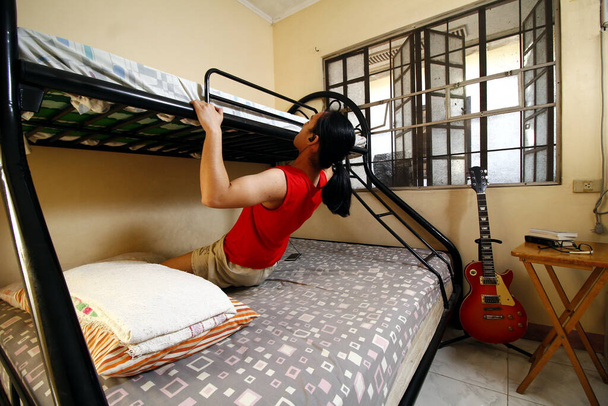 Zdjęcie młodego Azjaty ćwiczącego na łóżku bunkra podczas kwarantanny lub kwarantanny społecznej z powodu epidemii wirusa Covid 19 lub Corona. - Zdjęcie, obraz