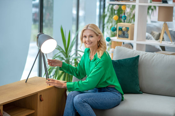 Donna bionda in una camicetta verde seduta vicino alla lampada
 - Foto, immagini