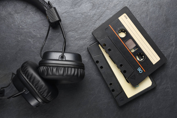 Fekete on-ear fülhallgató és audio szalag kompakt kazetták pala háttér - Fotó, kép