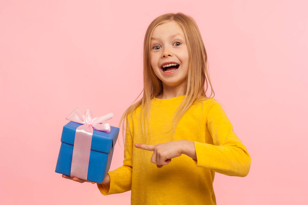 Portrait of delighted amazed little girl pointing gift box, boasting present and looking with astonishment to camera, shocked by birthday surprise. indoor studio shot isolated on pink background - Fotoğraf, Görsel