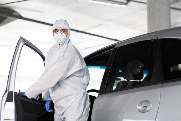 Ο άνθρωπος με τη στολή Hazmat να βγει από το αυτοκίνητο, coronavirus - Φωτογραφία, εικόνα