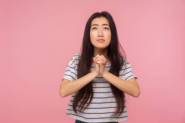 Please, I'm begging! Portrait of worried girl with long hair in t-shirt looking up and praying with imploring eyes, pleading for help, asking forgiveness. studio shot isolated on pink background - Φωτογραφία, εικόνα