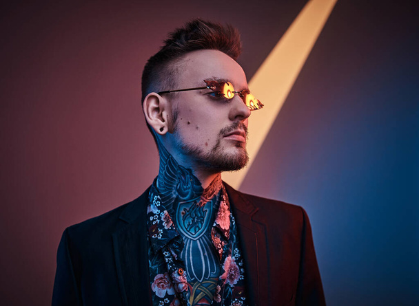 Tatuointi taiteilija mies malli poseeraa neon studio puolialaston tatuoitu elin, smokki ja aurinkolasit
. - Valokuva, kuva
