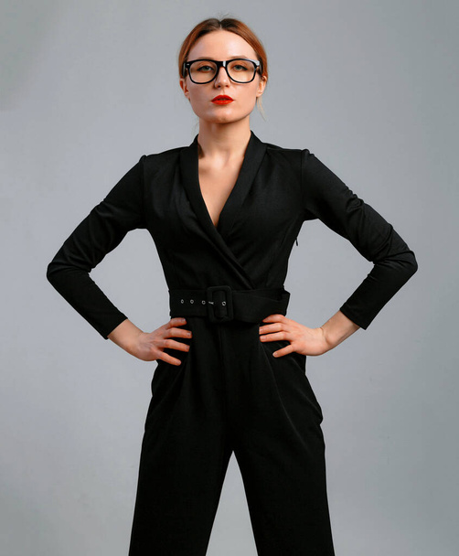 elegant business woman in black classic overalls and glasess posing over gray background. Happy satisfied relaxed elegant woman enjoy her work - 写真・画像