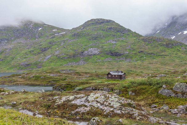 traditional norwegian wooden house standing at the lakeside and mountains in the distance, selective focus. - 写真・画像