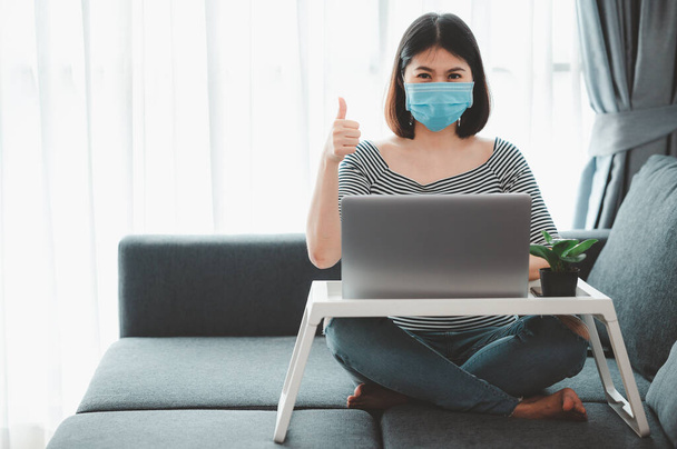 Жінка з Азії, одягнена в маску обличчя, працює вдома під час коронавірусного карантину, показуючи пальцем вгору - Фото, зображення