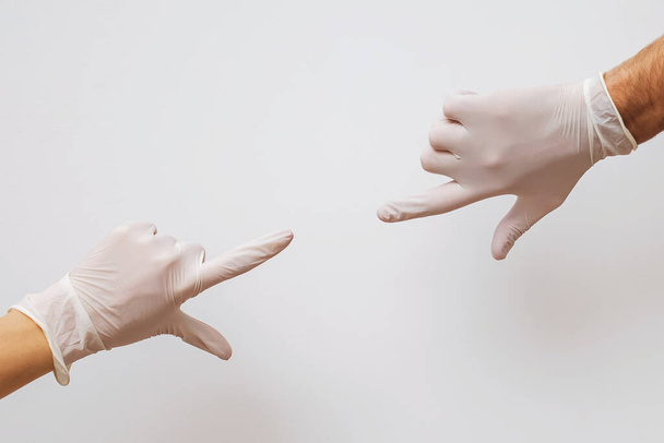 Twee handen bedekt met rubberen handschoenen die naar elkaar toe reiken - Foto, afbeelding