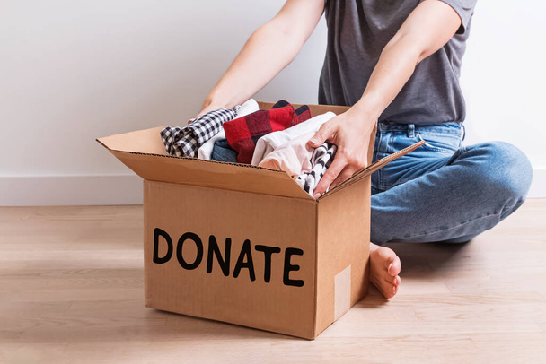 Woman putting her clothes in a carboad box with text Donate written on it. - Foto, Bild