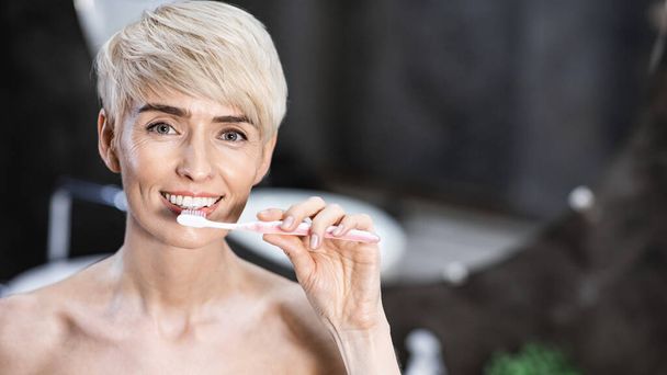 女性の歯をきれいにするパノラマのバスルームでカメラに微笑む - 写真・画像