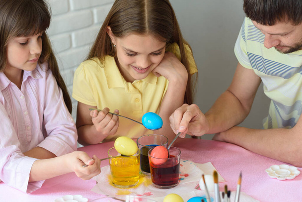 Daddy paint eggs in glasses with colorful dyes. - Foto, Bild