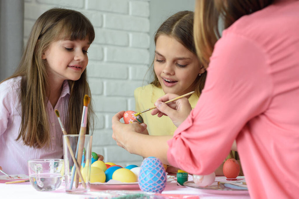 Mamá muestra a las niñas cómo pintar huevos de Pascua maravillosamente
 - Foto, imagen