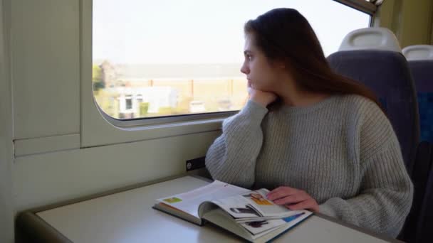 Eine schöne junge Frau fährt mit dem Zug und liest ein Buch, eine junge Frau blickt traurig aus dem Fenster - Filmmaterial, Video