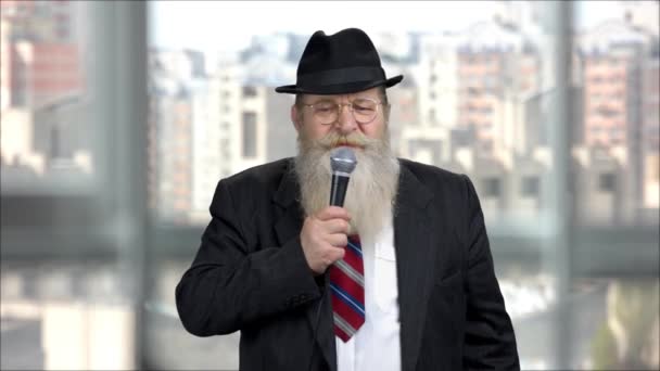 Senior long-bearded man giving speech with microphone indoor. - Footage, Video